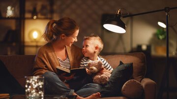 Mutter liest ihrem Sohn auf der Couch unter dem Schein einer Stehlampe eine Geschichte vor. 
