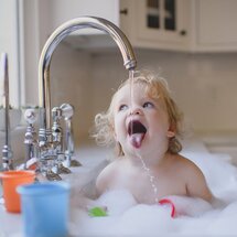 Lachendes Kleinkind sitzt im Spülbecken und spielt mit Schaum in einem modernen Haushalt