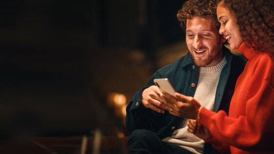 Junges Paar lacht gemeinsam beim Blick auf das Handy und nutzt digitale Energieangebote