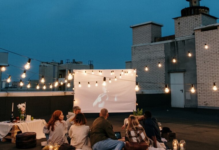 Gruppe Jugendlicher schaut bei Nacht auf einem Hausdach einen Film auf einer Leinwand