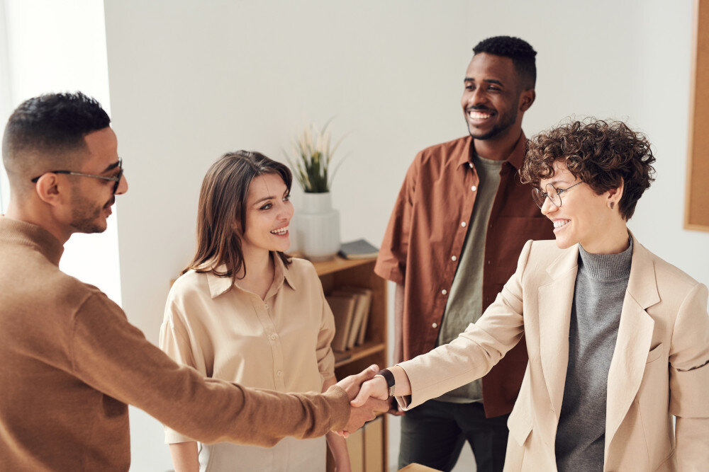 Eine gruppe von jungen Menschen in Businesskleidung steht zusammen, die zwei Personen im Vordergrund geben sich die Hand. | © pexels-fauxels-3184416