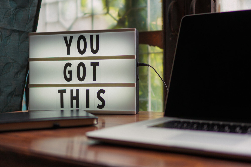 Laptop steht auf einem Holztisch neben einem Motivationsschild mit der Aufschrift ‚You got this‘