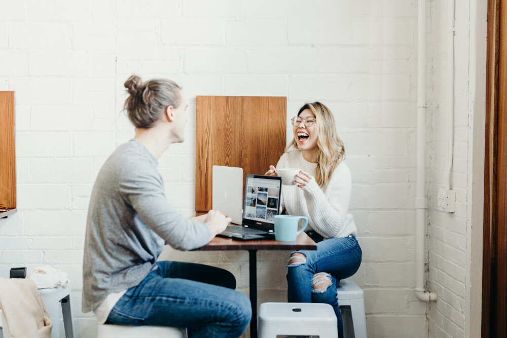 Zwei Kollegen sitzen gemeinsam in einer Kaffeeküche und lachen bei der Pause. | © brooke-cagle-TxSVqNgnjq4-unsplash
