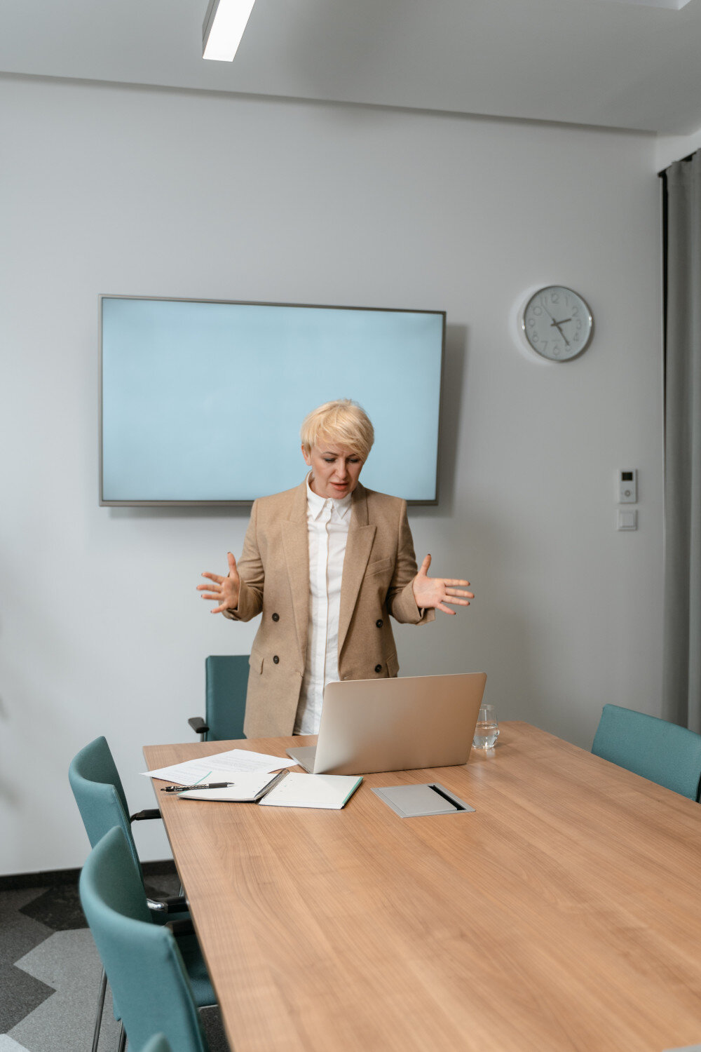 Eine Businessfrau hält vor einer digitalen Zuhörerschaft eine Präsentation vor ihrem Laptop. Im Hintergrund an der Wand hängt eine Uhr damit sie die Zeit nicht vergisst. | © pexels-mart-production-7222974