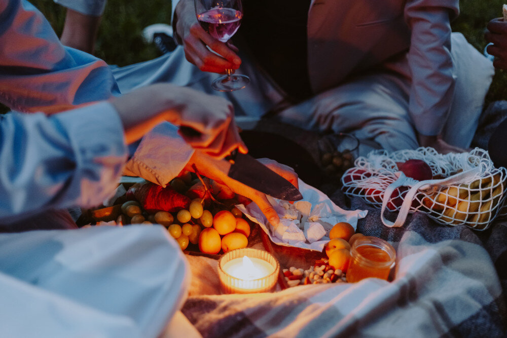 Abgebildet ist eine Picknick-Decke mit Leckereien und Kerzenlicht in der abendlichen Dämmerung.  | © pexels-cottonbro-studio-10071283