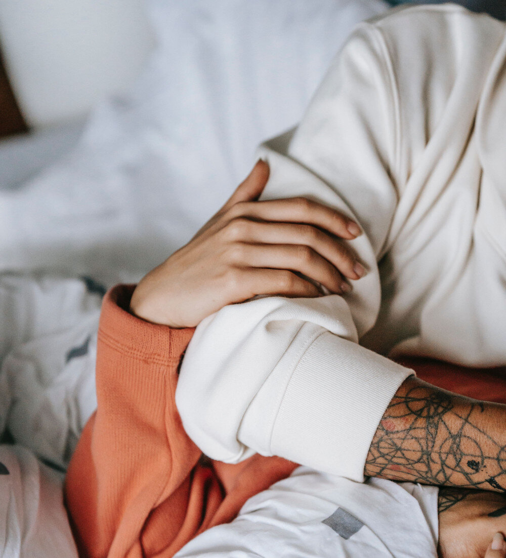 Ein Pärchen liegt im Bett, die Arme miteinander verschlungen. Ein Partner/eine Partnerin trägt Tattoowierungen auf der Hand, die gehalten wird.  | © pexels-tim-samuel-5838268