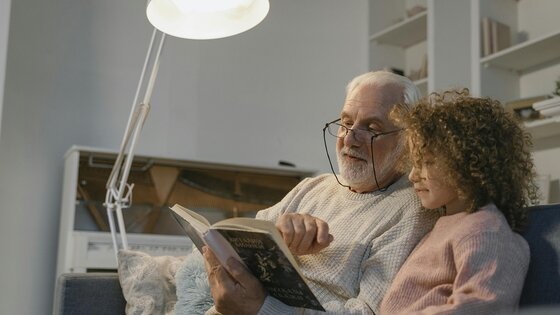 Ältere Menschen lesen gemeinsam auf dem Sofa, beleuchtet von einer Stehlampe
