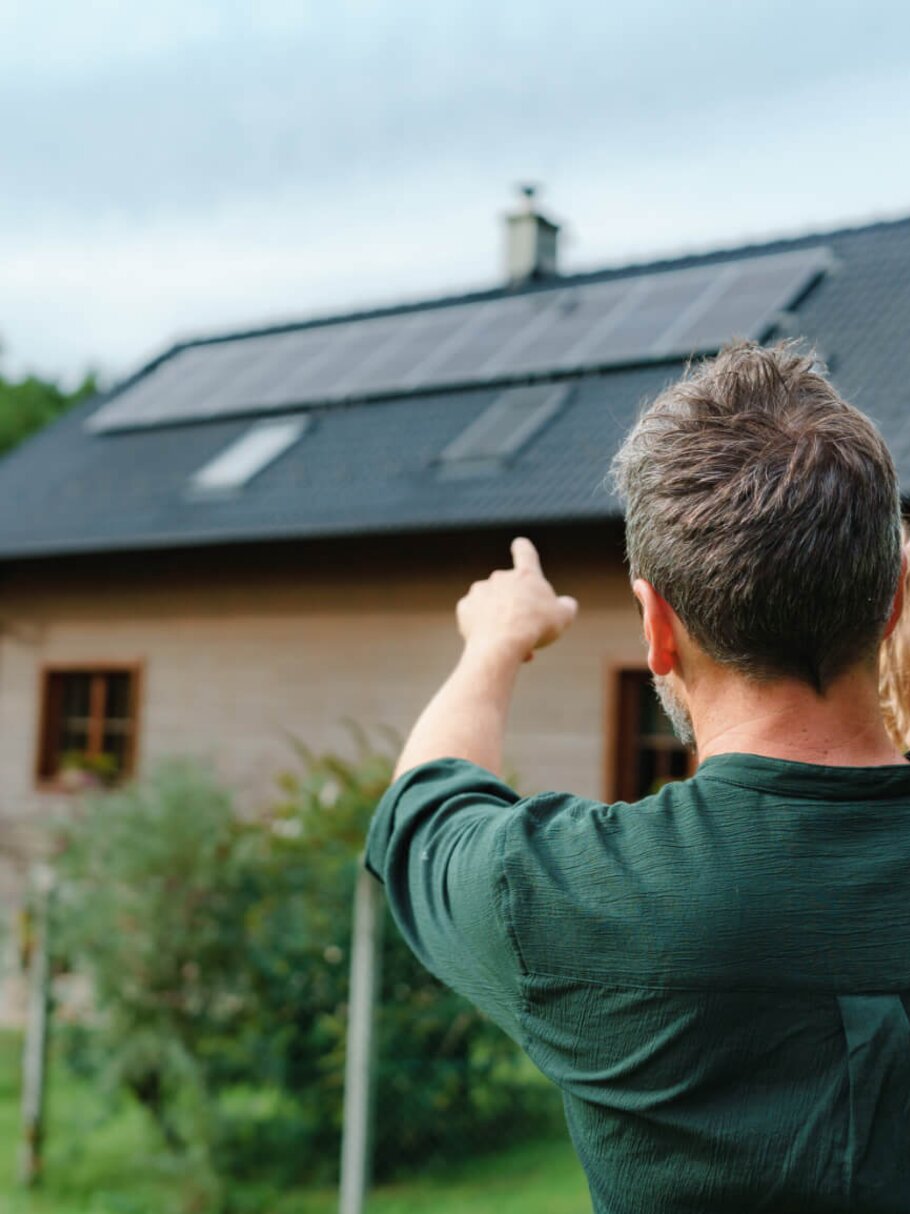 Vater hält kleines Mädchen in den Armen vor ihrem Haus mit Photovoltaikanlage