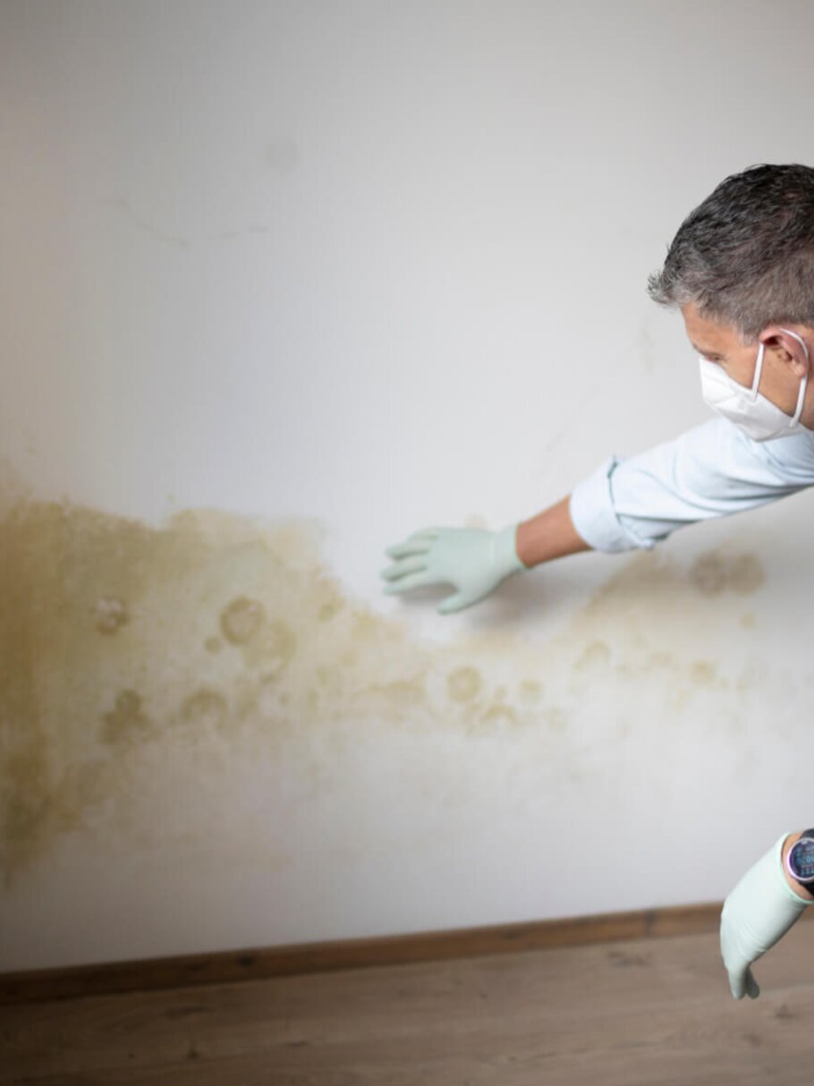 Mann mit Mund-Nase-Maske vor Wand mit Schimmel