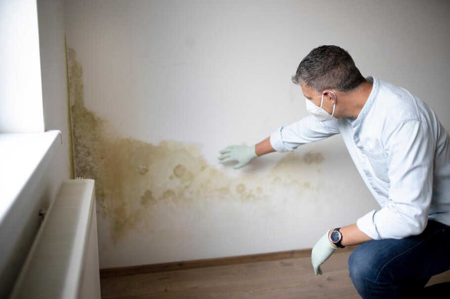 Mann mit Mund-Nase-Maske vor Wand mit Schimmel