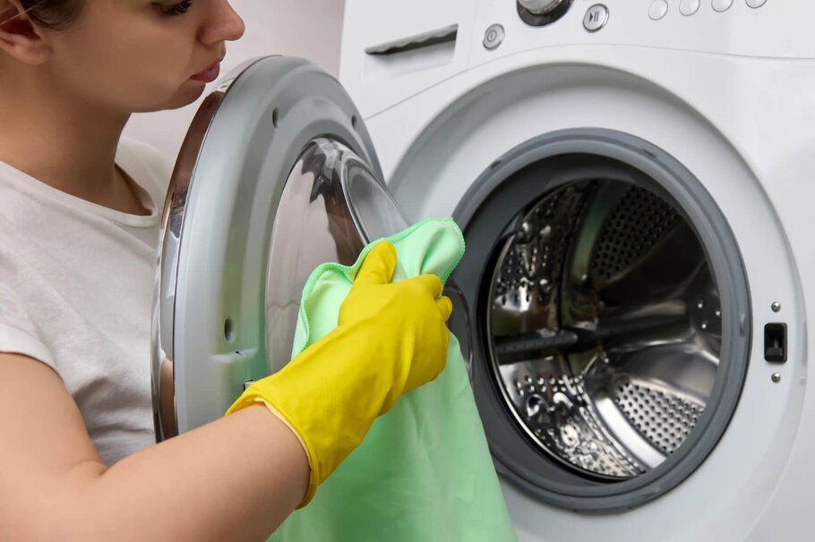 Frau mit gelben Handschuhen reinigt Waschmaschine 