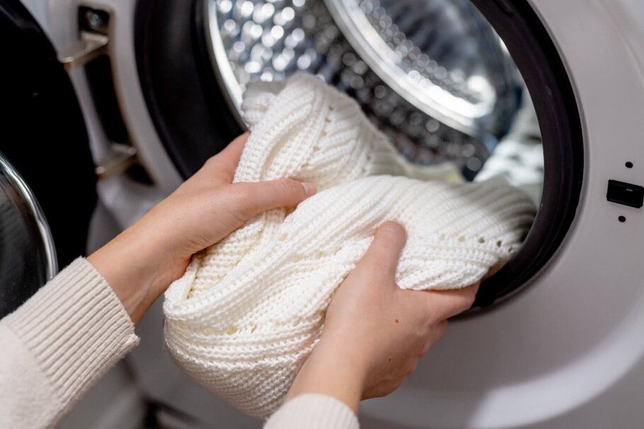 Frau nimmt weißen Pullover aus Wäschetrockner heraus