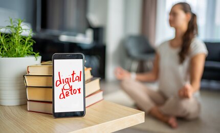 Digital detox - Frau meditiert im Hintergrund und lässt ihr Handy beiseite