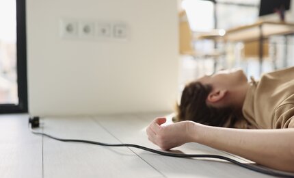 Person liegt am Boden neben einer Steckdose – Darstellung eines Stromunfalls