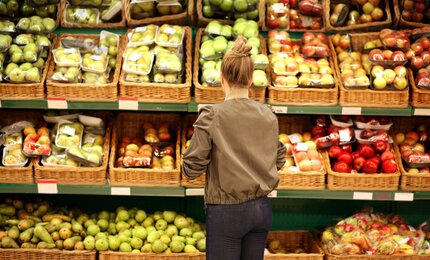 Frau vor Supermarktregal kauft Obst und Gemüse